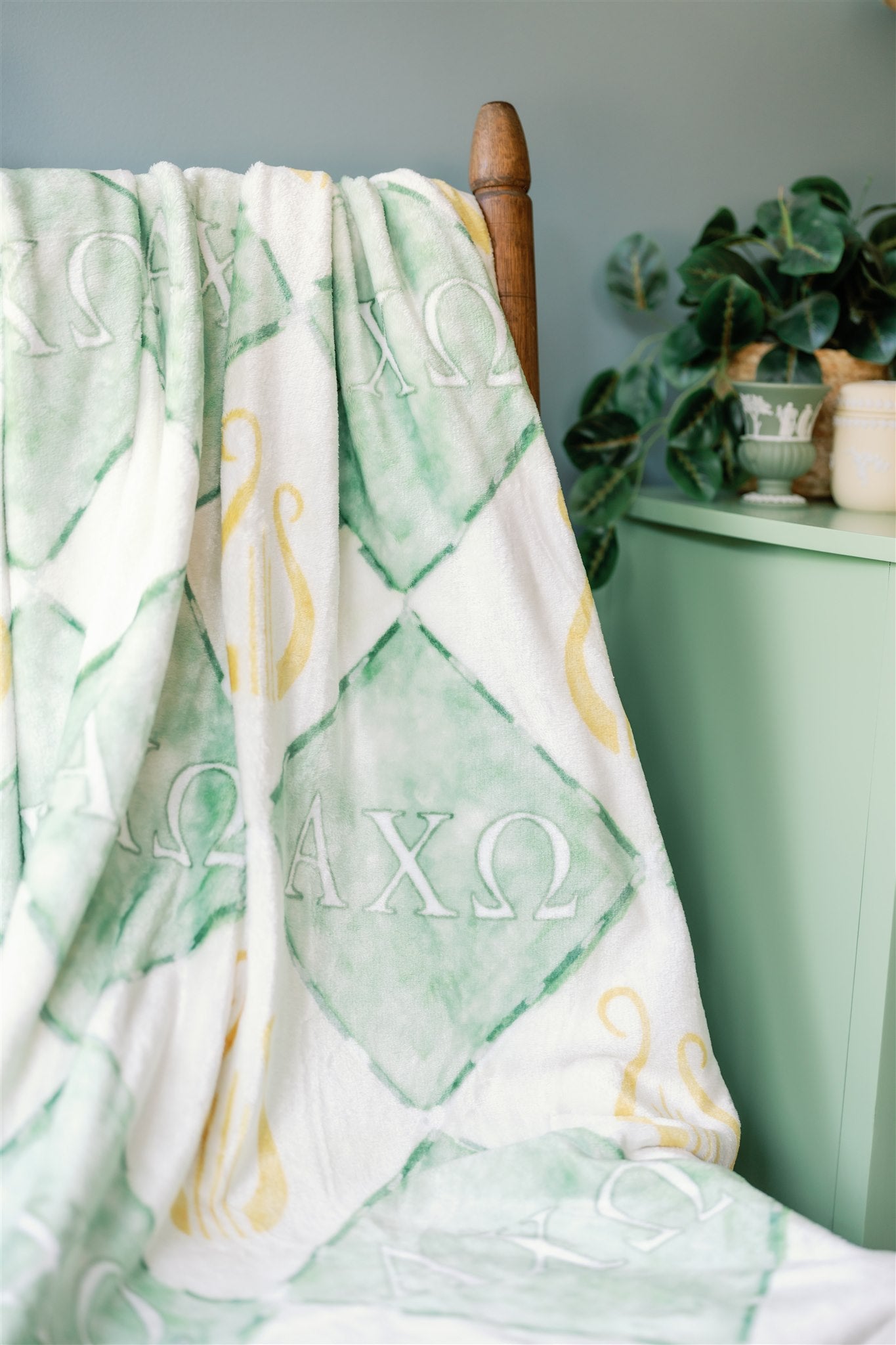 Blanket with Greek letters draped over a wooden chair against a light blue wall.
