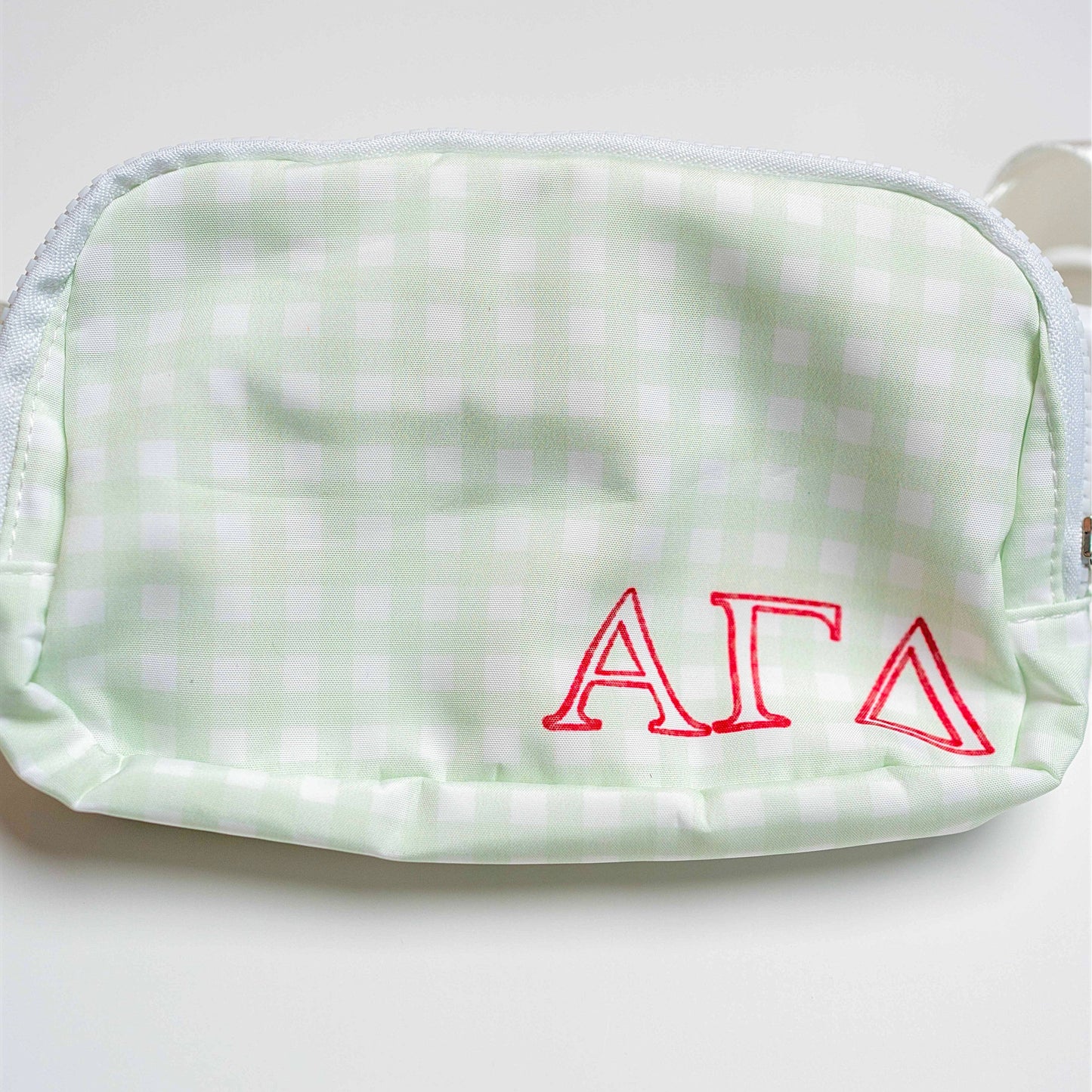 Light green gingham pouch with red Alpha Gamma Delta letters on a white background