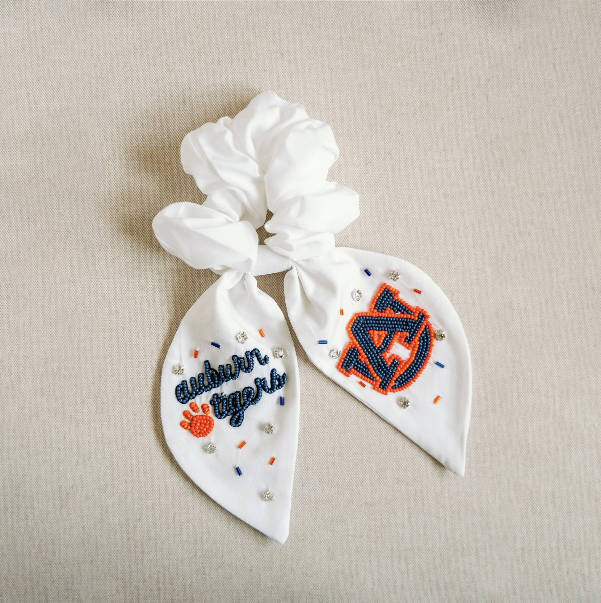 White scrunchie with two ribbons featuring beading of the Auburn logo and "Auburn Tigers."