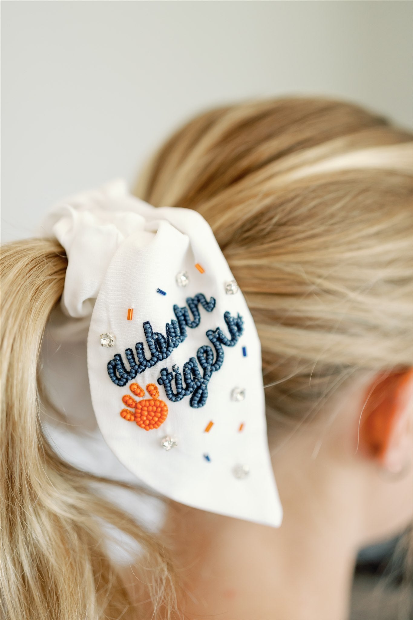 White scrunchie with two ribbons featuring beading of the Auburn logo and "Auburn Tigers."
