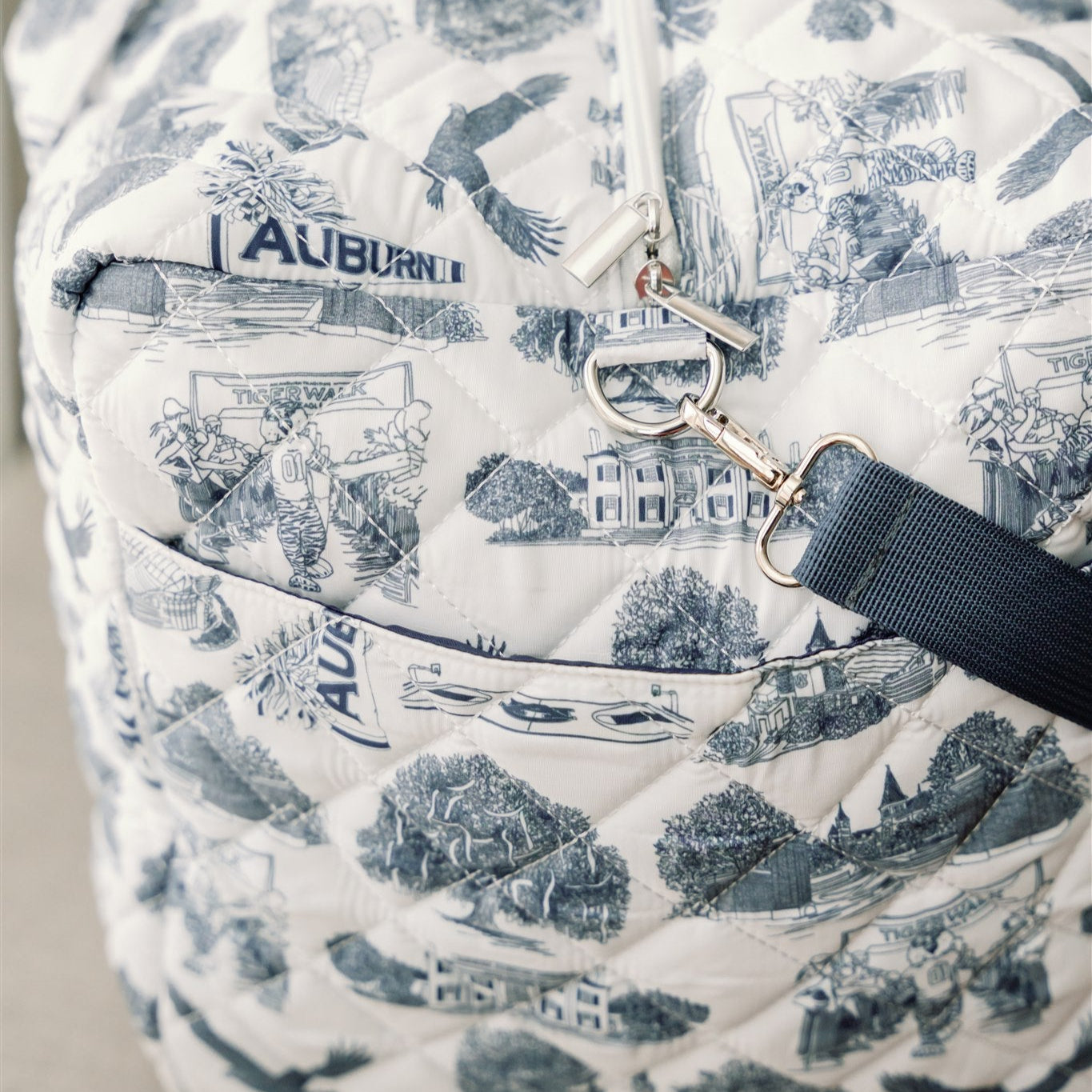 White quilted duffle bag with a navy strap and navy Auburn symbols.