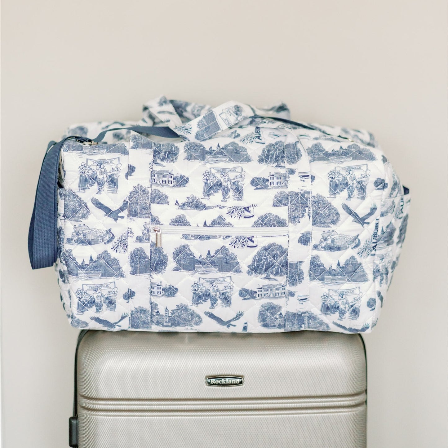White quilted duffle bag with a navy strap and navy Auburn symbols.