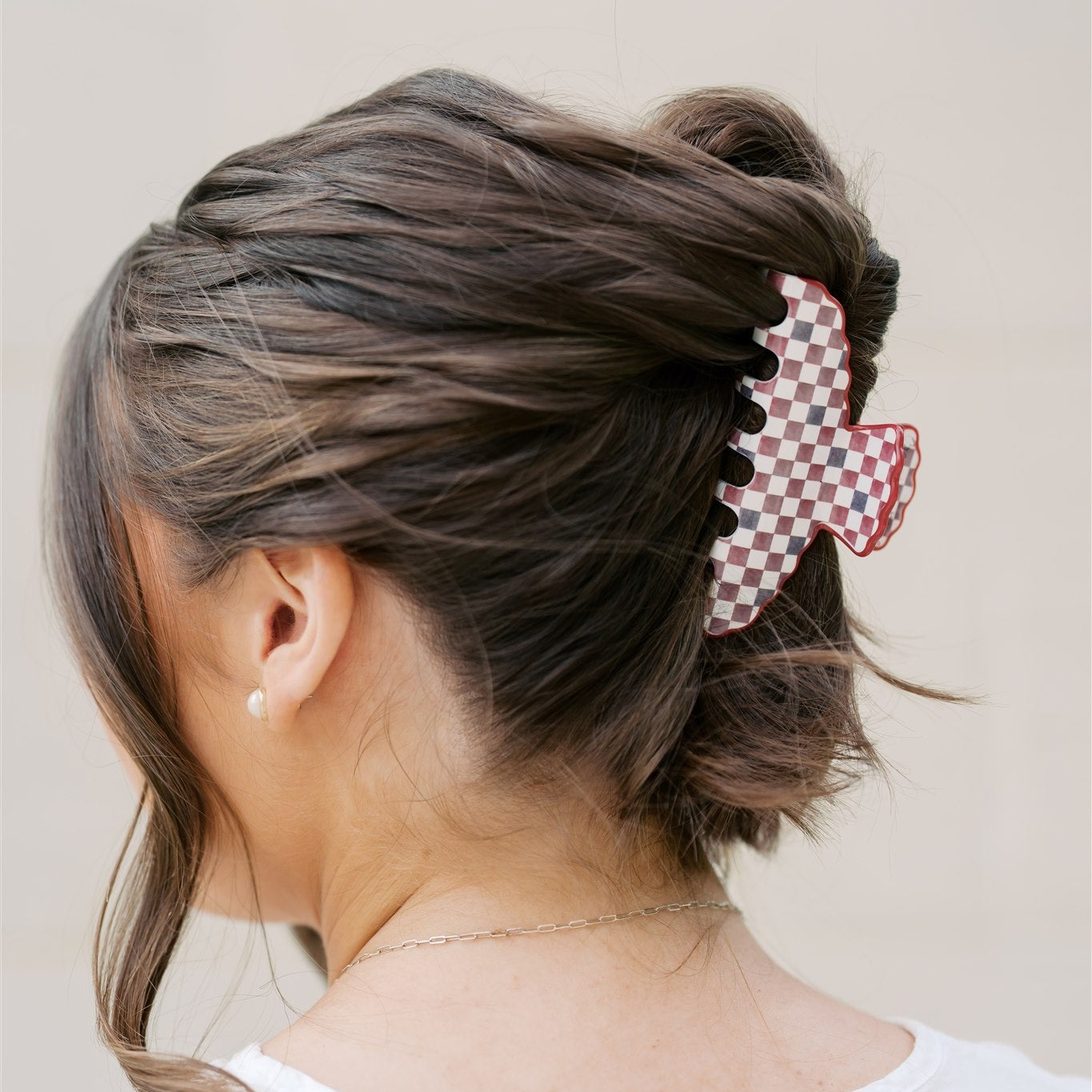 Back view of a person with styled hair featuring a checkered hair clip on a plain background