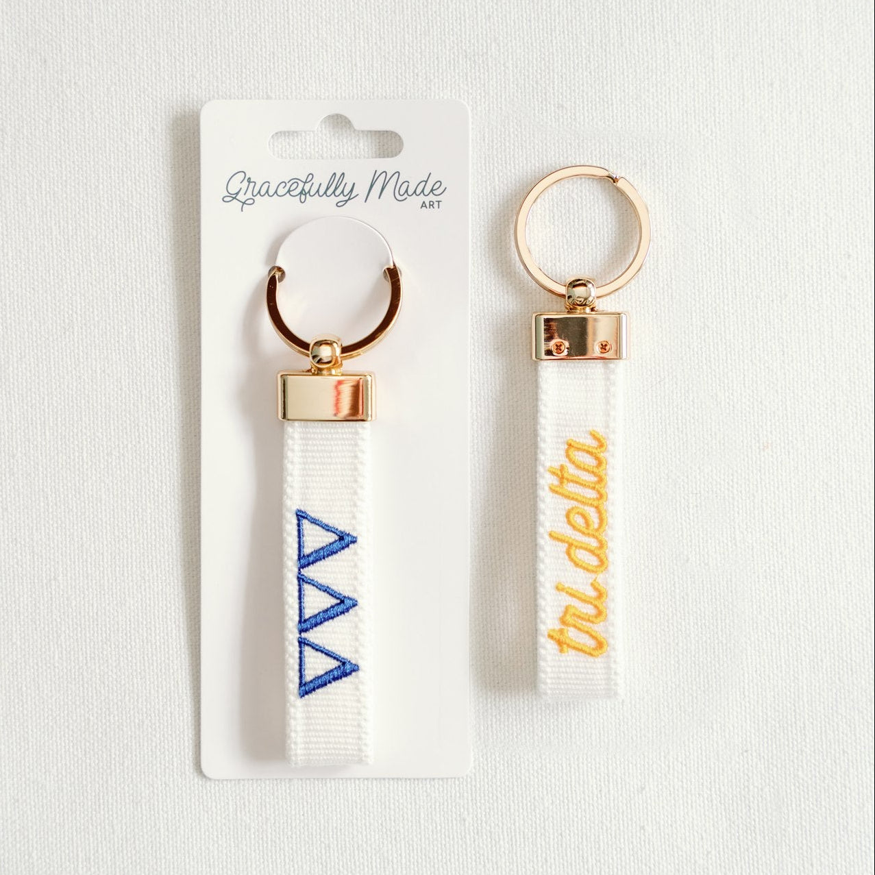 Front and back of a white keychain with Tri Delta Greek letters embroidered on it and Gracefully Made Art branded packaging.