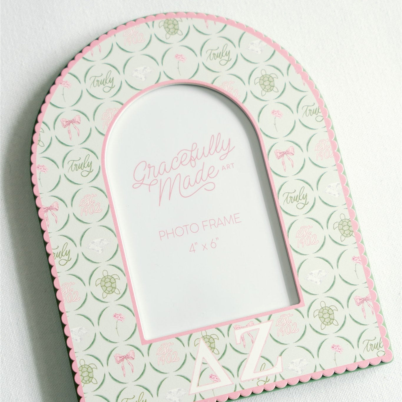 Close up of a pink and green photo frame with Delta Zeta pattern and greek letters on a white background.