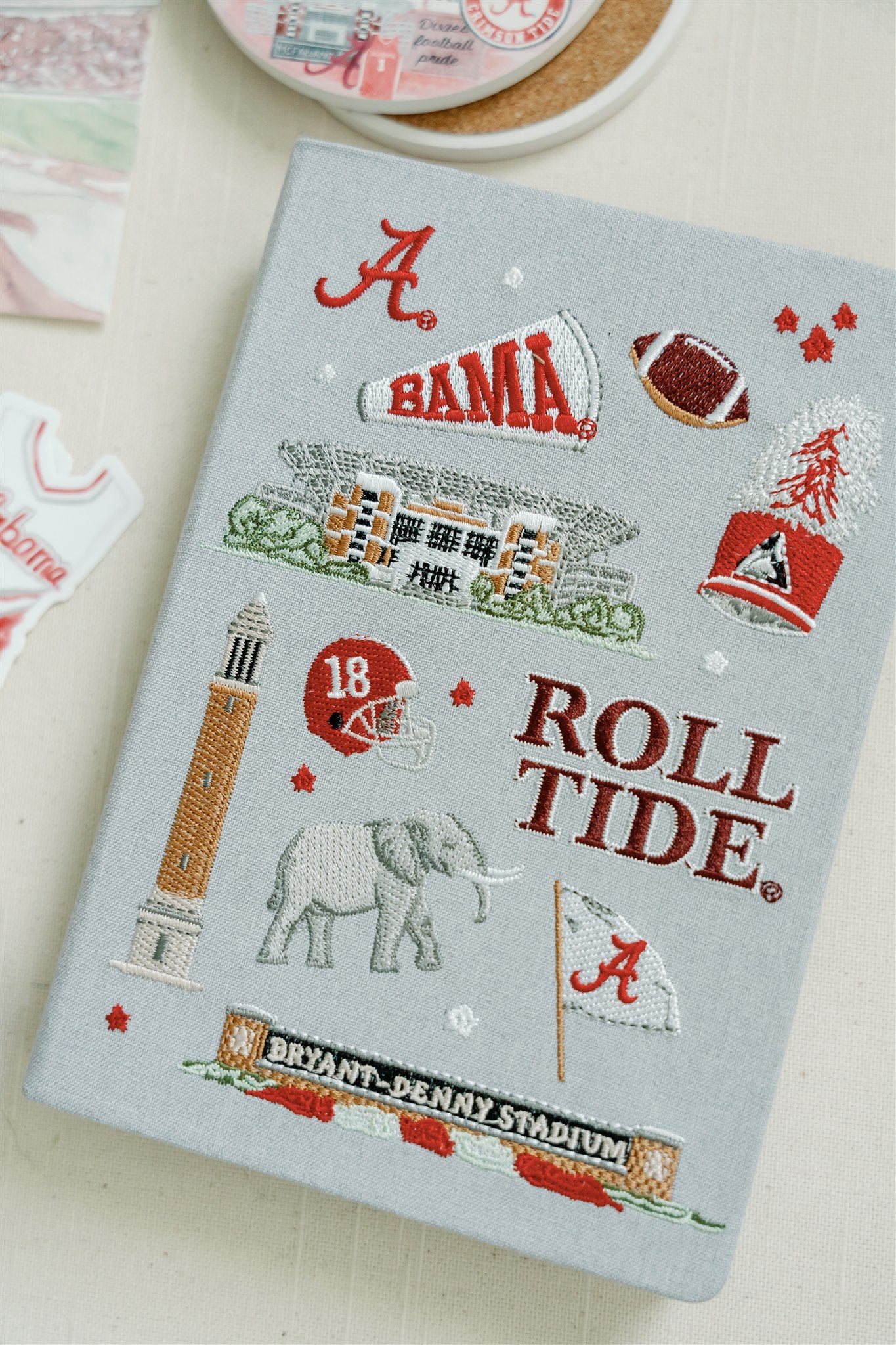 Light grey hardcover notebook with embroidered University of Alabama symbols on the front.