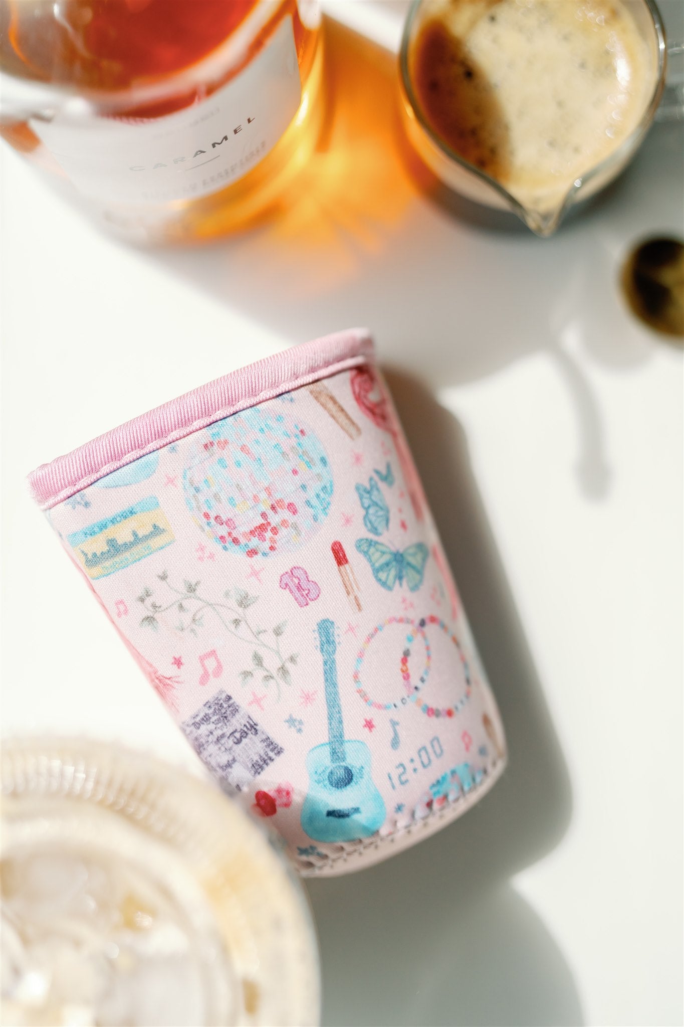 Light pink coffee sleeve with watercolor Taylor Swift inspired symbols.