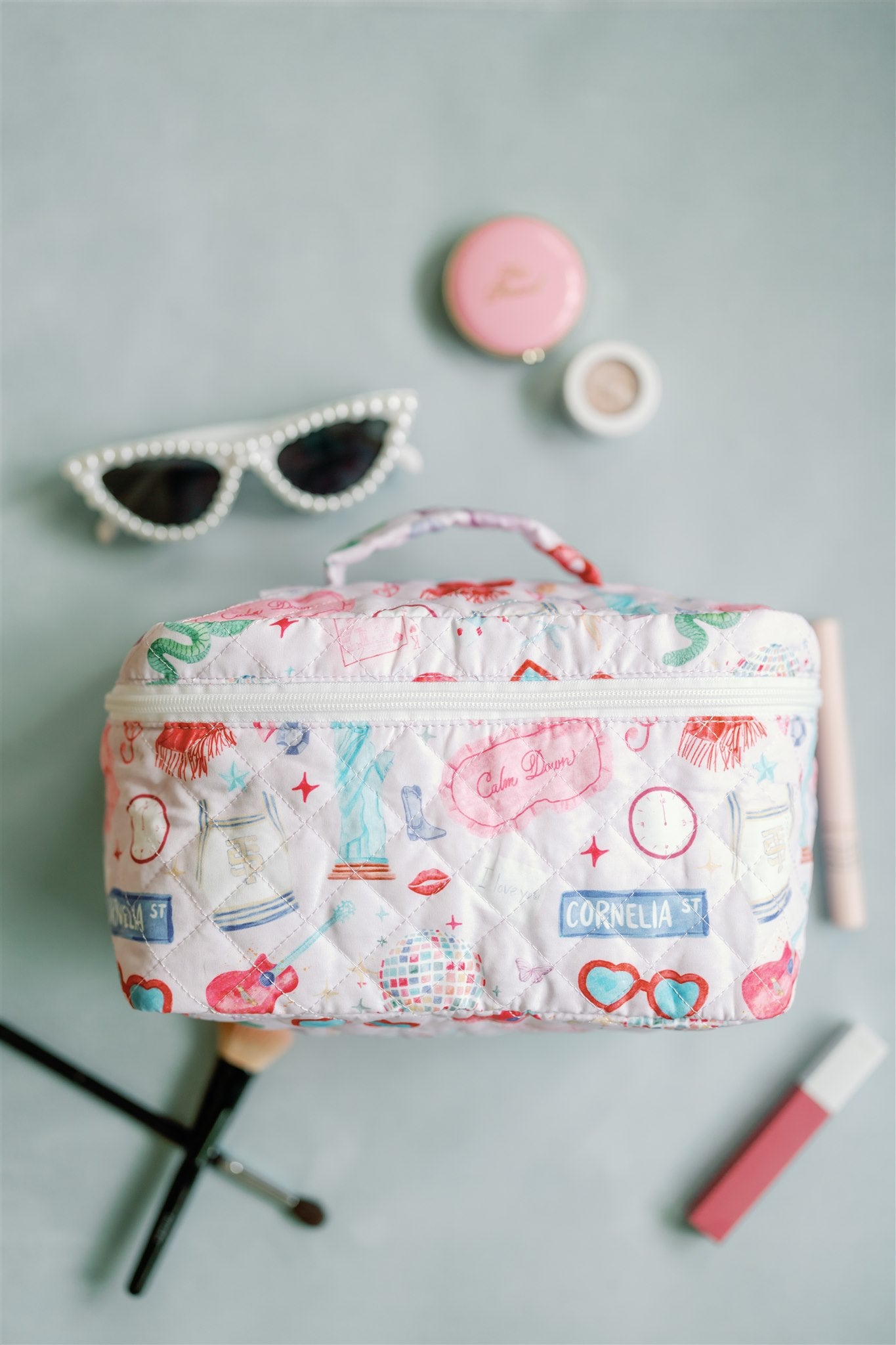 Quilted makeup bag with a pattern featuring original watercolor illustrations of Taylor Swift icons.