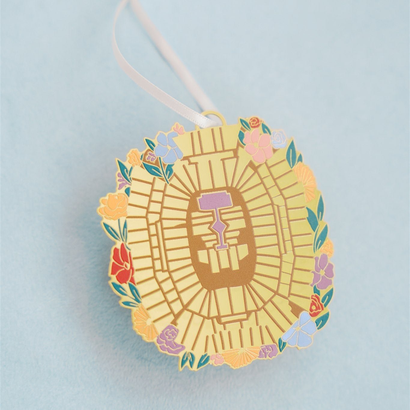 Christmas ornament of the Taylor Swift Eras Tour stadium from an aerial view with flowers around it.