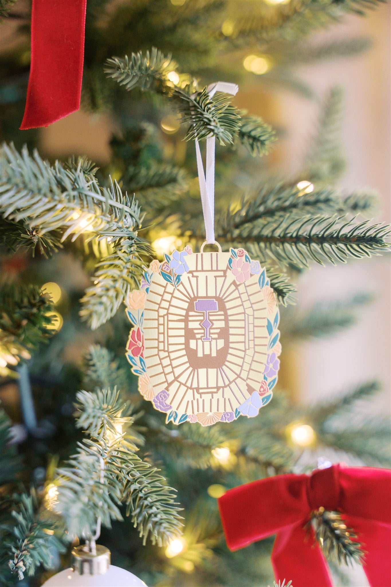 Christmas ornament of the Taylor Swift Eras Tour stadium from an aerial view with flowers around it.