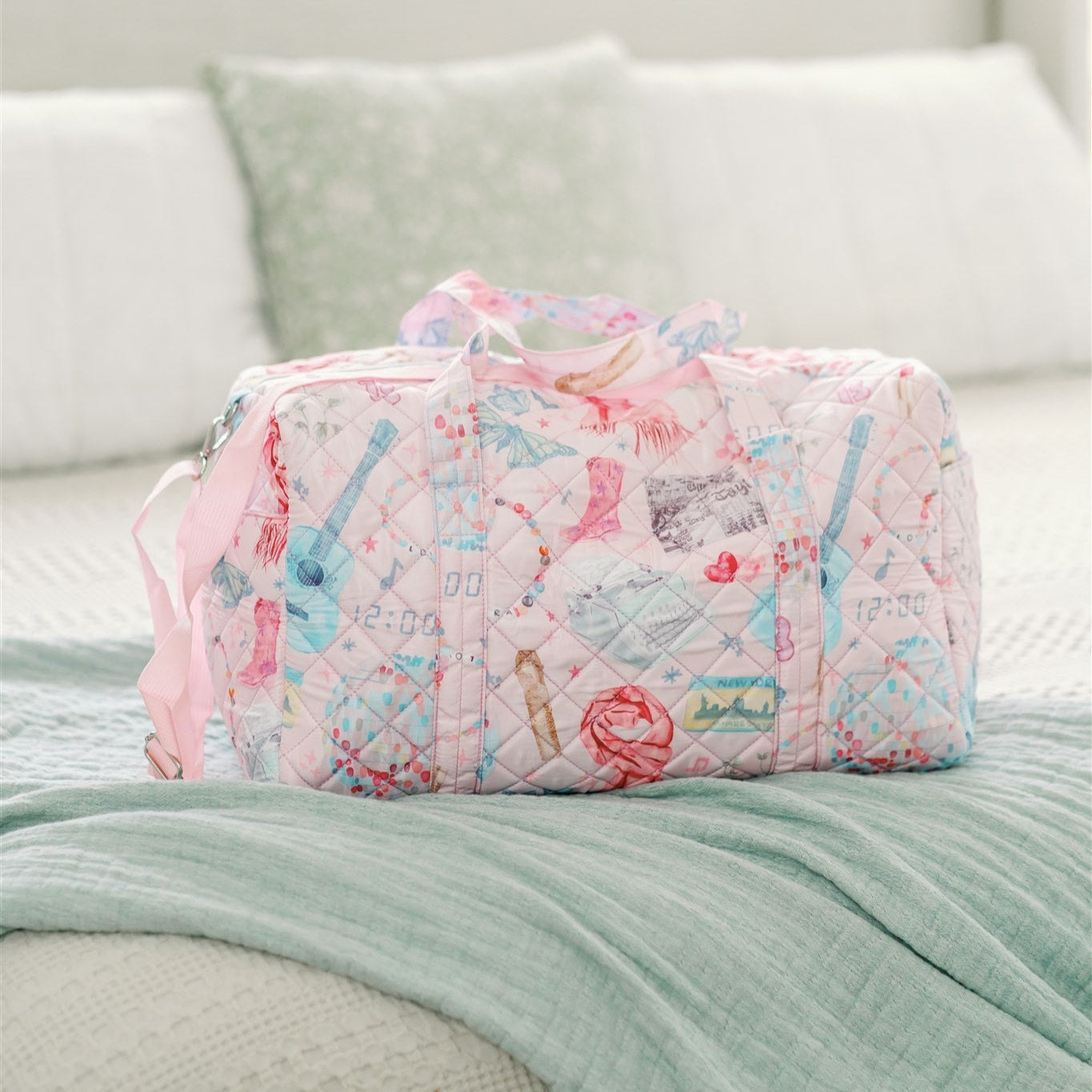 Light pink quilted duffle with 2 handles, a strap, and a pattern featuring original watercolor art of Taylor Swift icons.