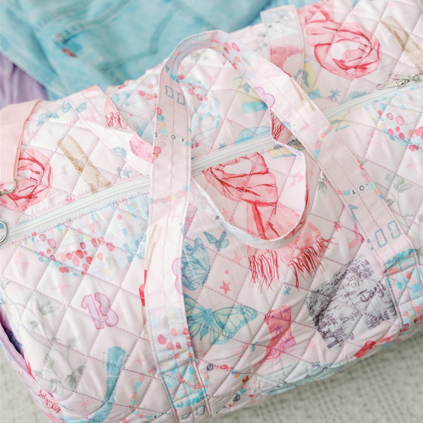Light pink quilted duffle with 2 handles, a strap, and a pattern featuring original watercolor art of Taylor Swift icons.