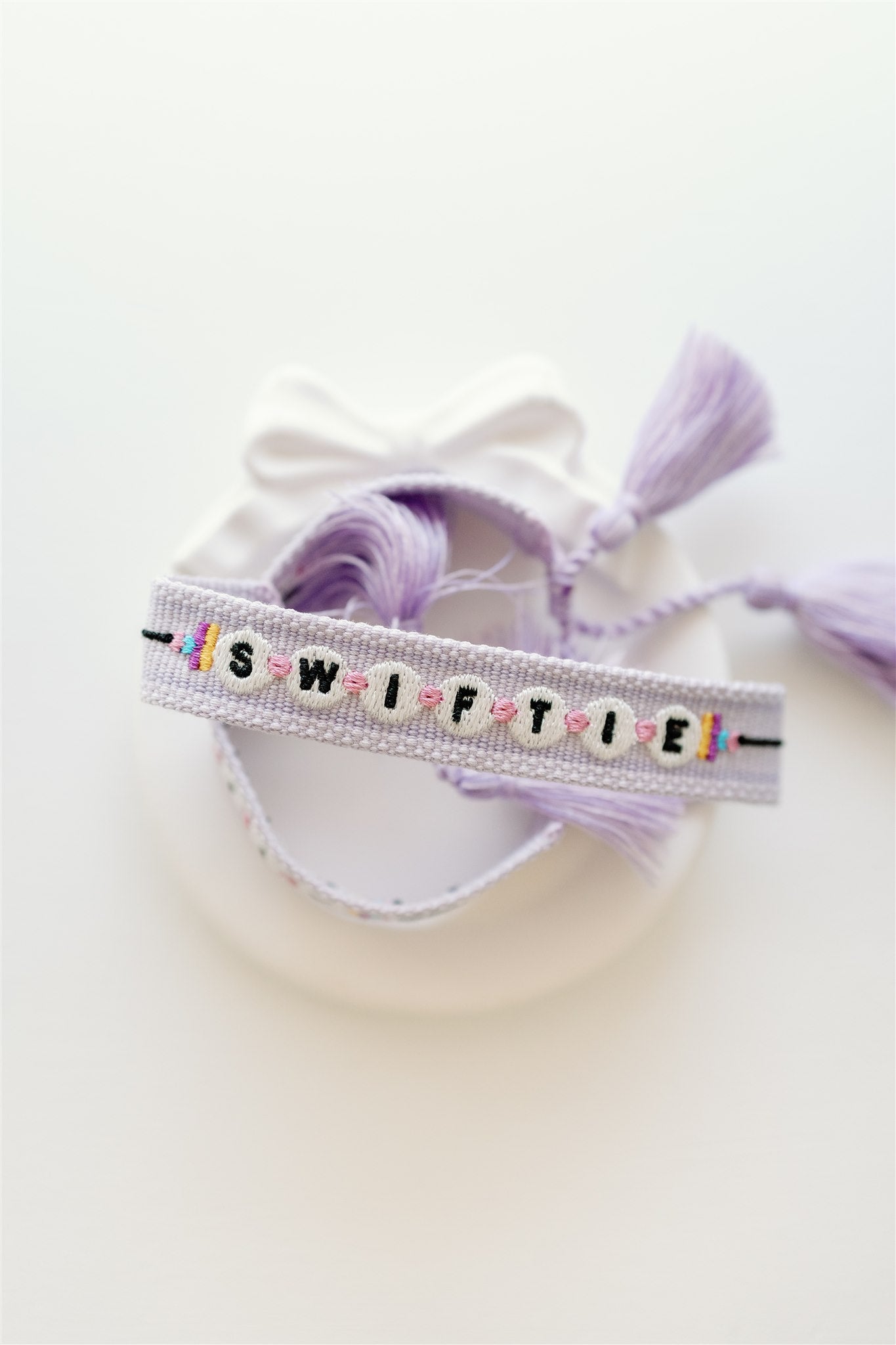 Light purple woven bracelet with "Swiftie" on it in a pattern that resembles beads.