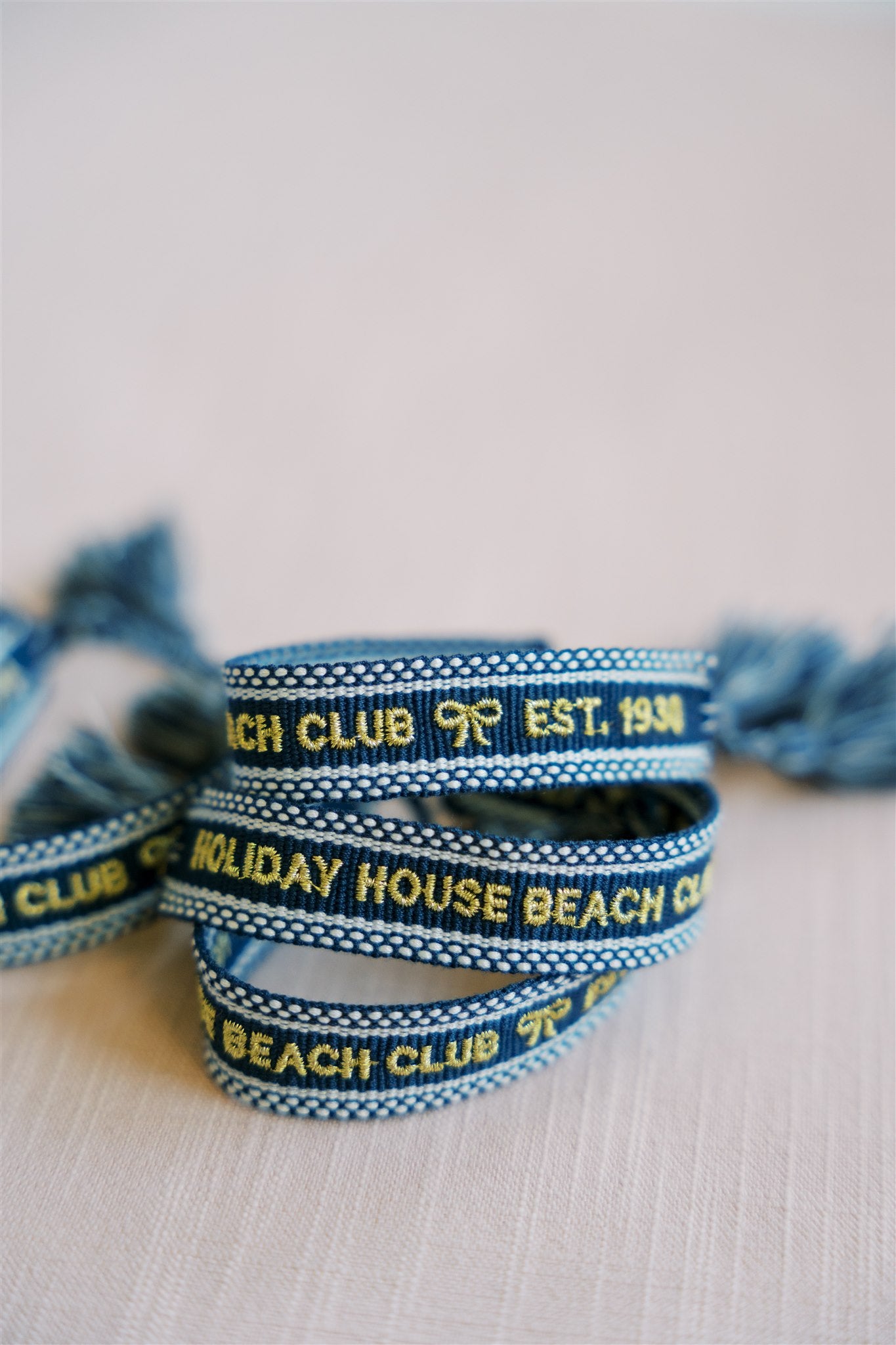 Navy blue woven bracelet with "Holiday House Beach Club est.1930" written on it in gold.