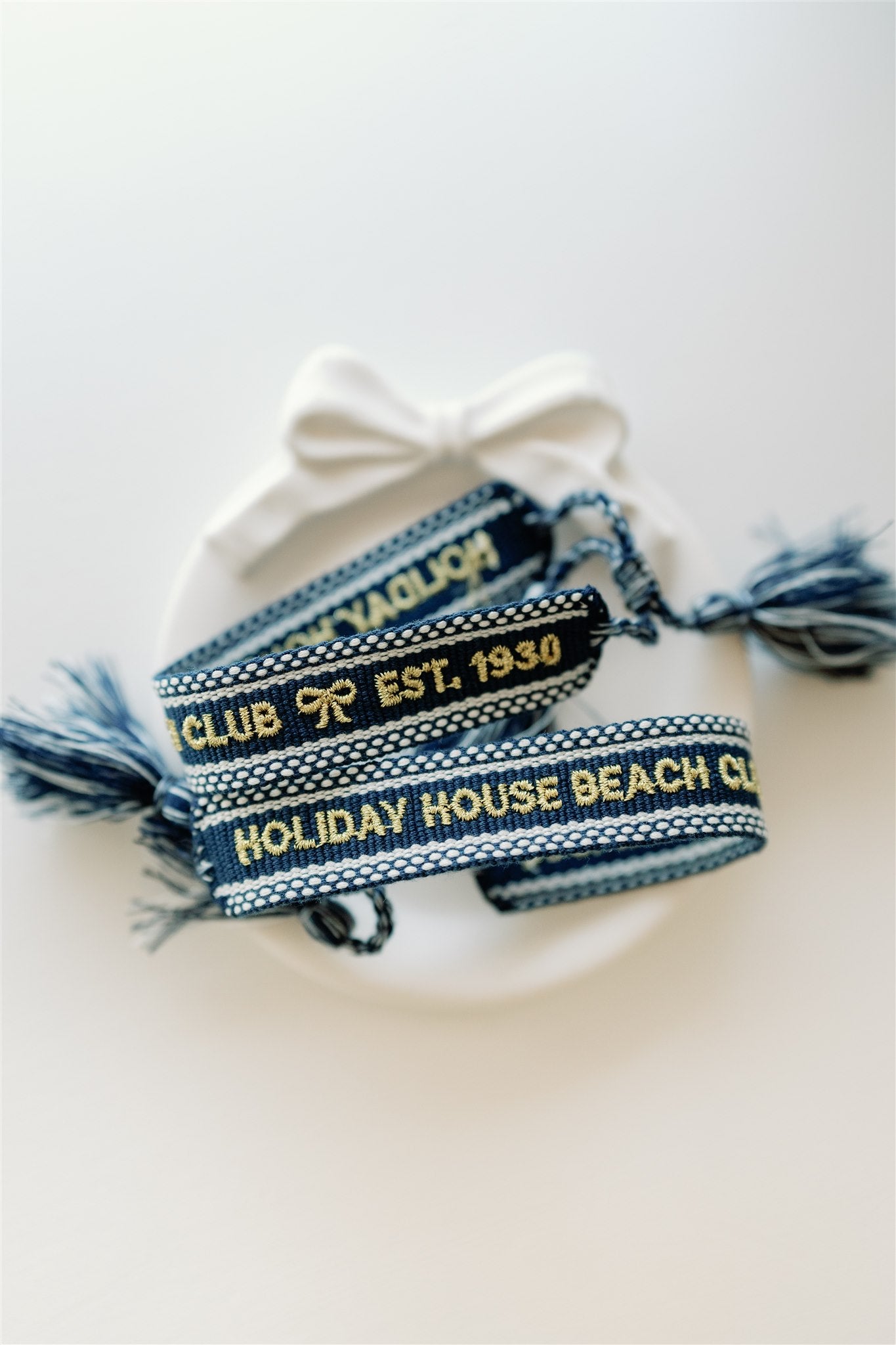 Navy blue woven bracelet with "Holiday House Beach Club est.1930" written on it in gold.
