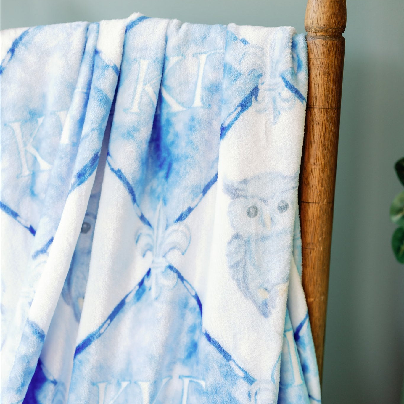 Blue and white patterned blanket draped over a wooden chair with Kappa Kappa Gamma branding.