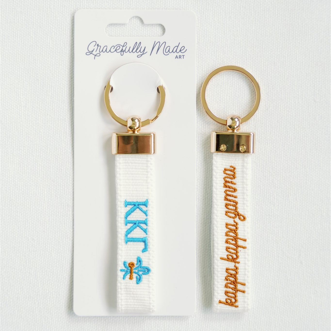 Front and back of a white keychain with KKG and Kappa Kappa Gamma embroidered on it with branded packaging.