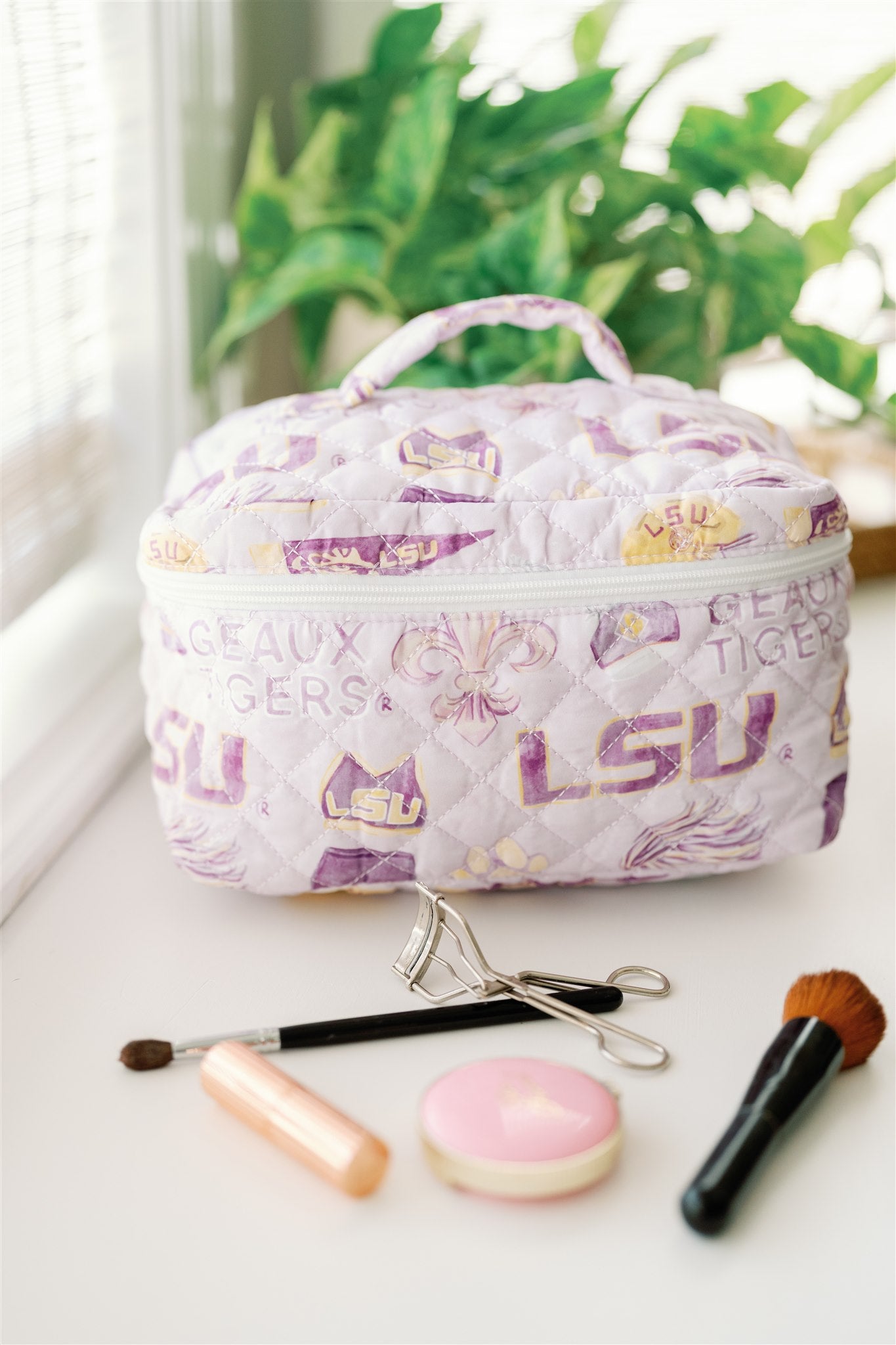 Light purple quilted make up bag with watercolor LSU symbols on it.