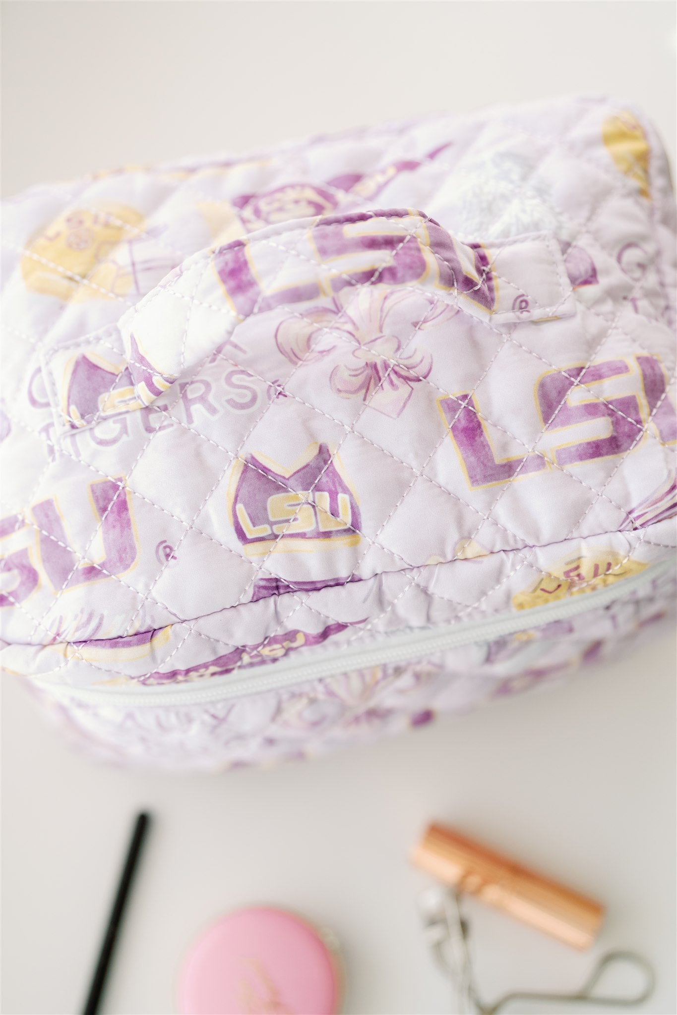 Light purple quilted make up bag with watercolor LSU symbols on it.