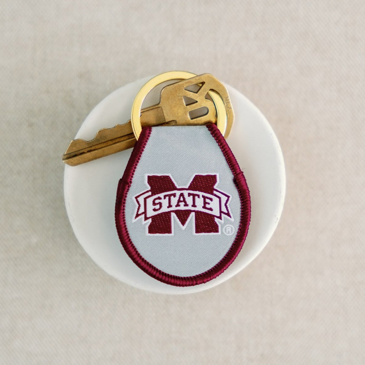 A light grey and maroon keychain with the Mississippi State logo embroidered on it.