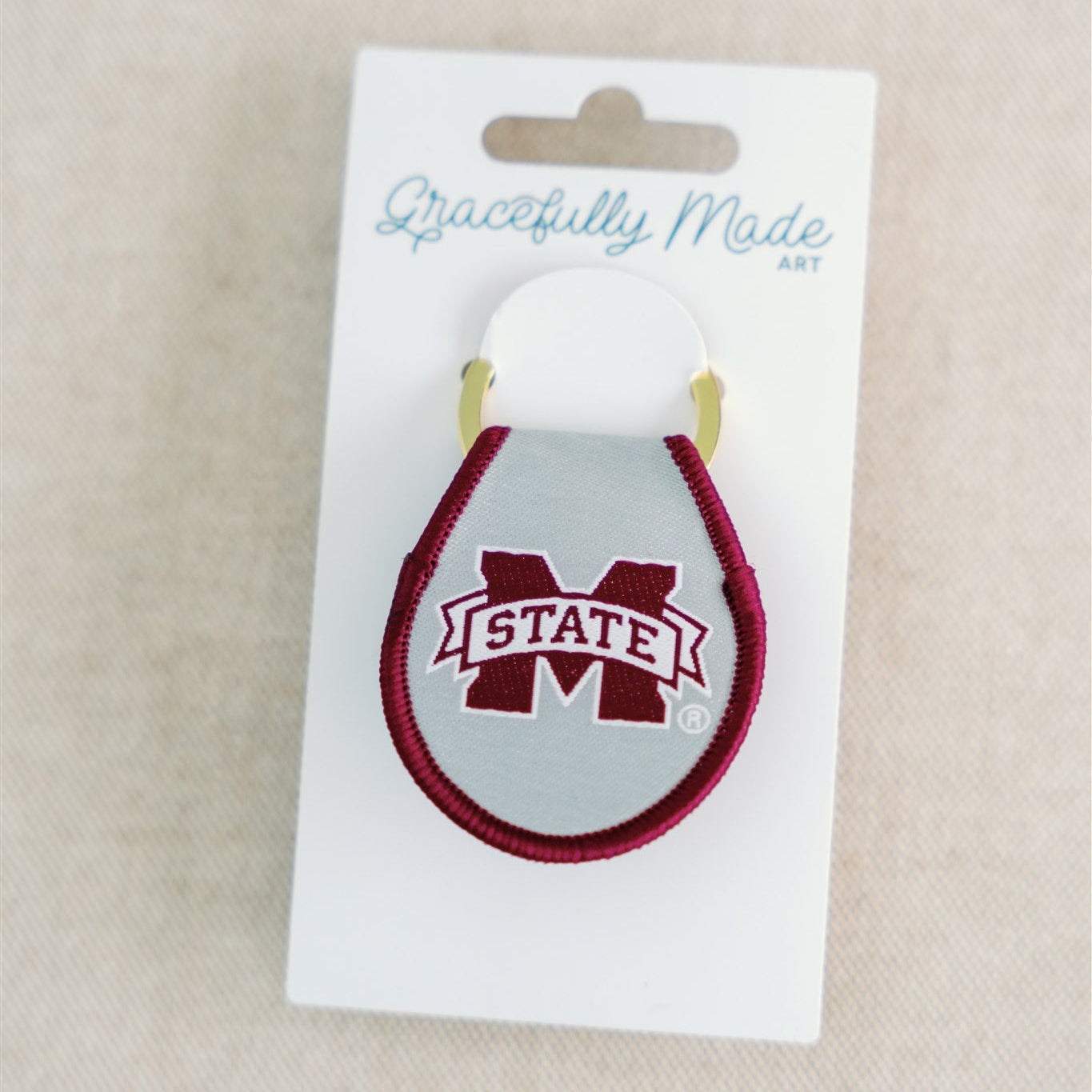 A light grey and maroon keychain with the Mississippi State logo embroidered on it.