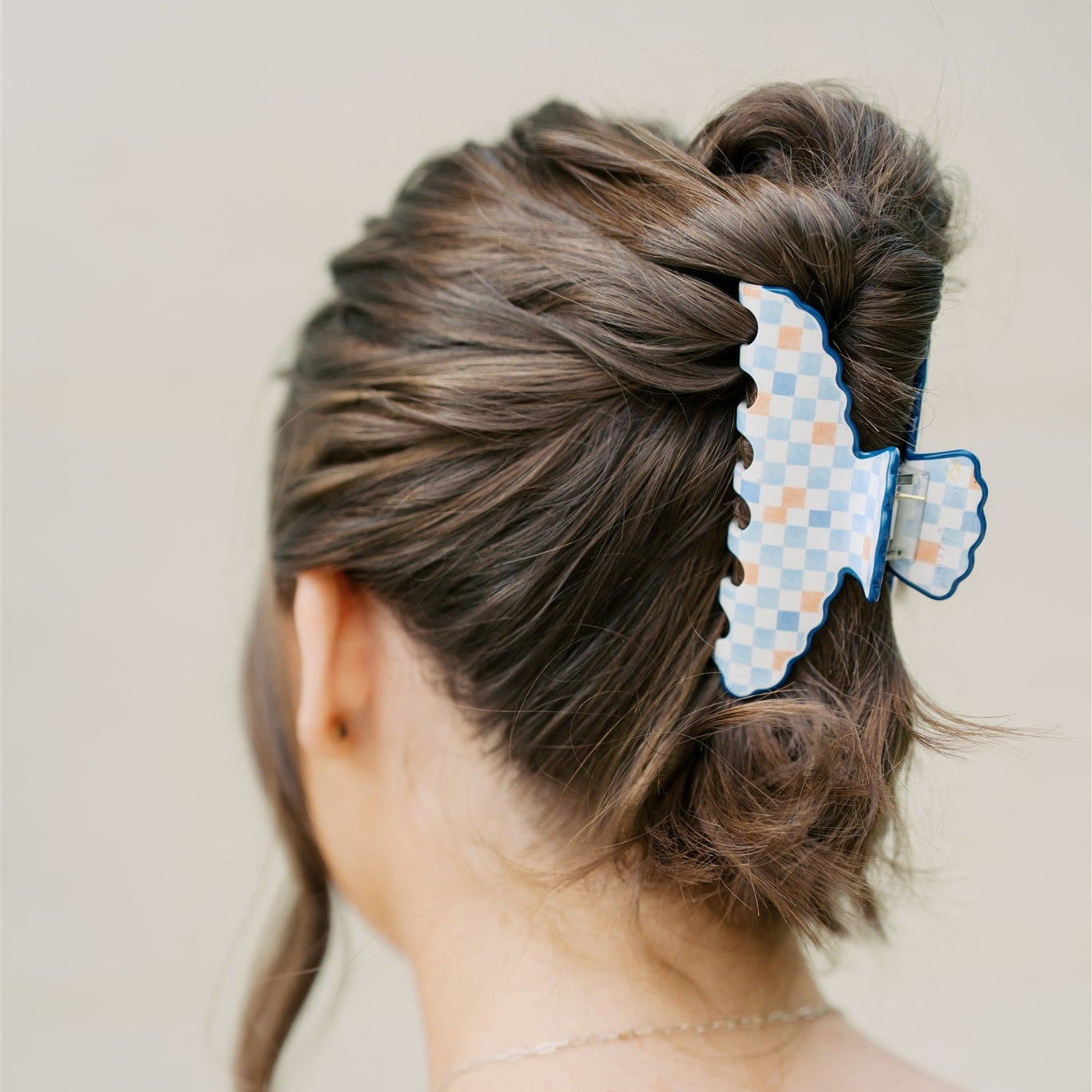 Person with a bun wearing a blue and orange checkered hair clip on a plain background