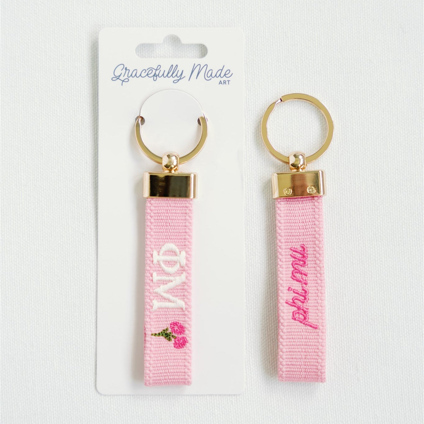 Two pink keychains with gold accents and Phi Mu Greek letters on a white background