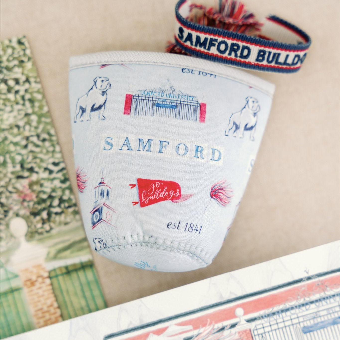 Light blue coffee sleeve with watercolor symbols themed to Samford University printed on it.