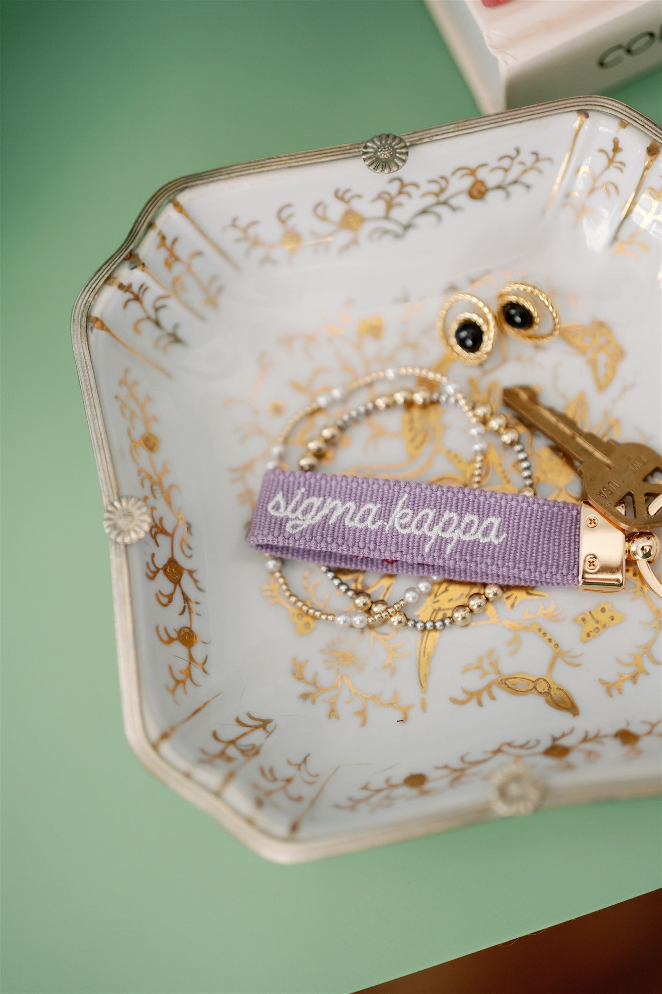 Decorative jewelry dish with 'sigma kappa' keychain and other accessories on a green background