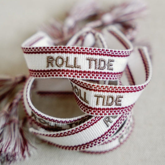 White and red woven bracelet with "Roll Tide" written down the middle.
