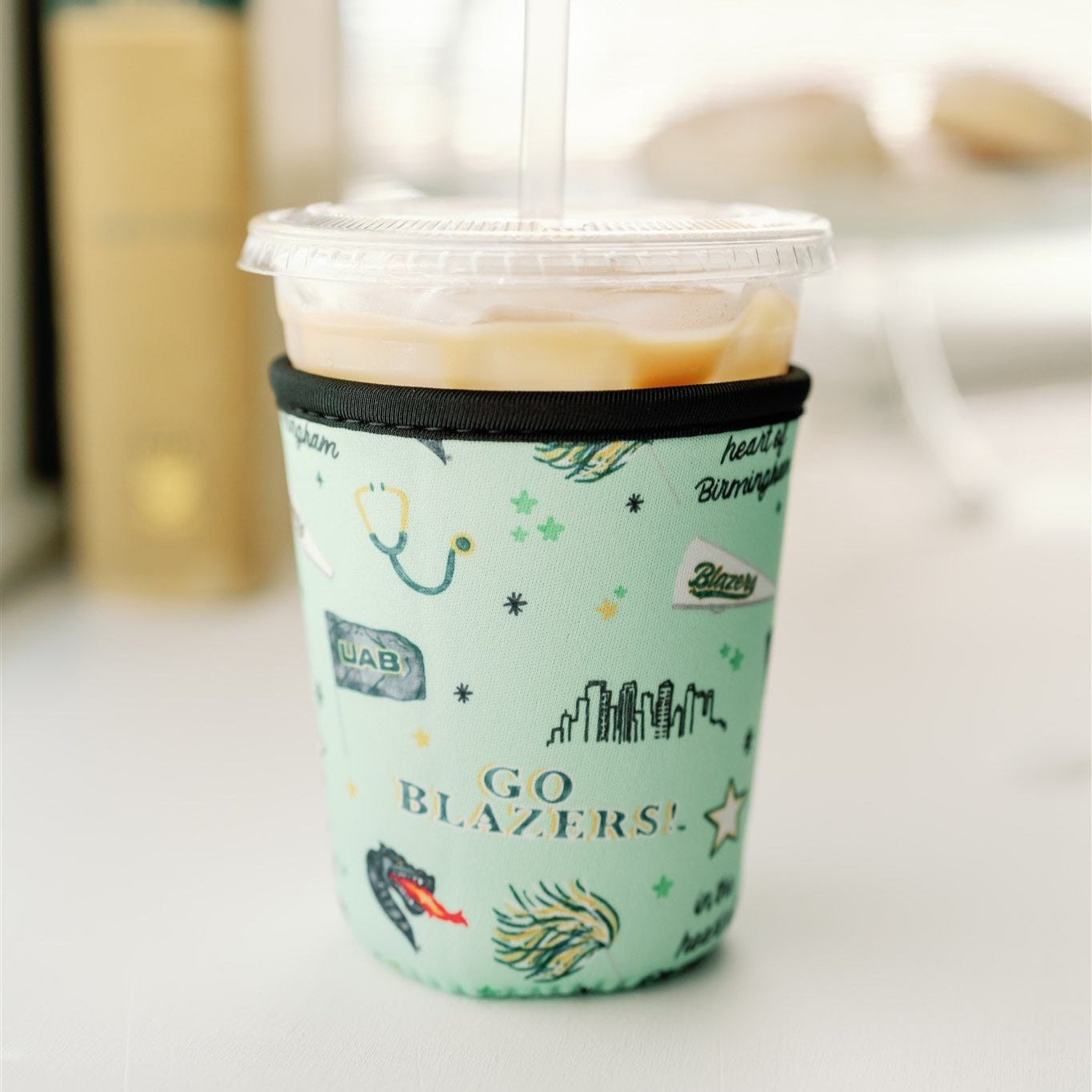 Light green coffee sleeve with watercolor UAB symbols on it.
