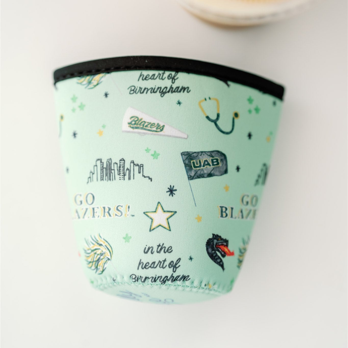 Light green coffee sleeve with watercolor UAB symbols on it.