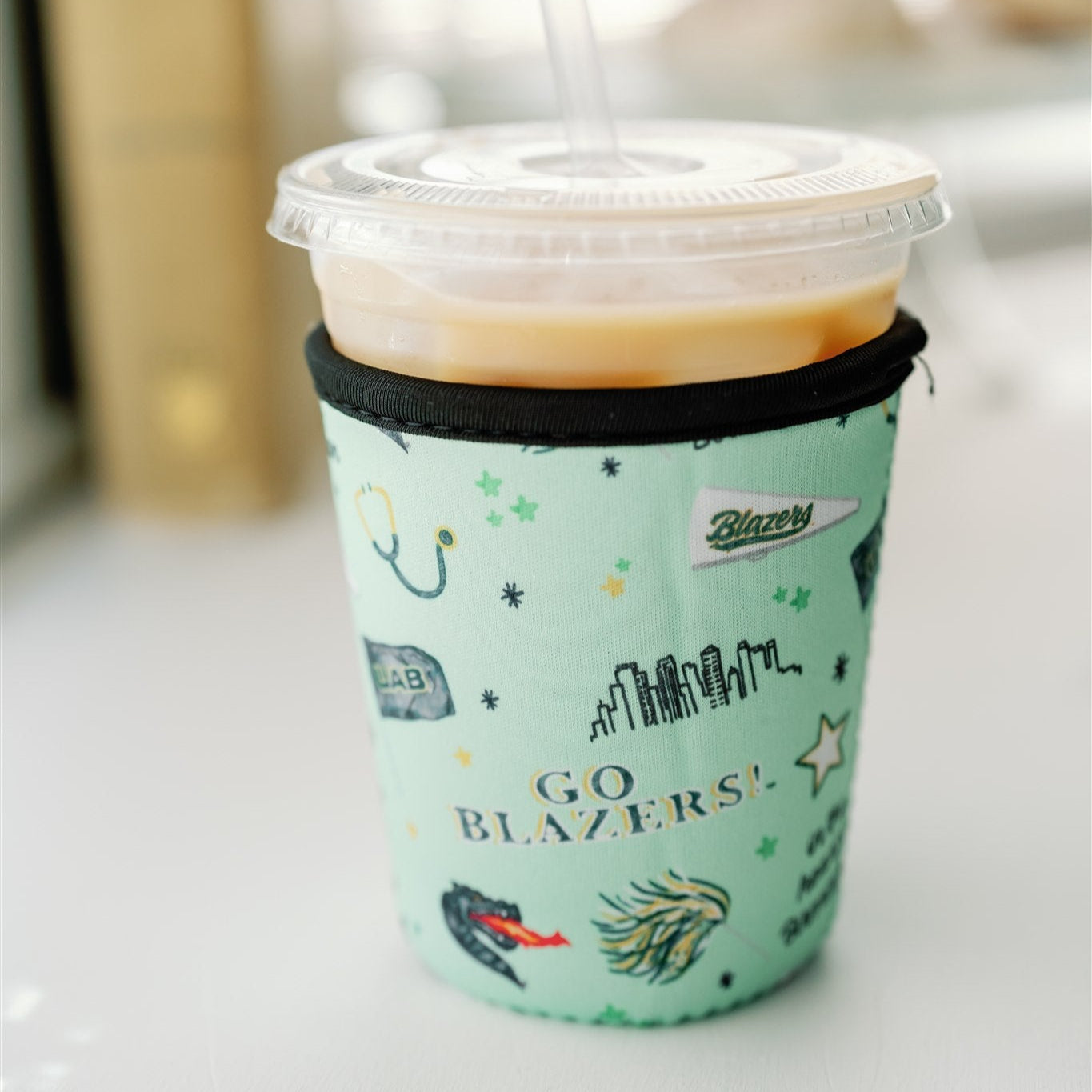 Light green coffee sleeve with watercolor UAB symbols on it.
