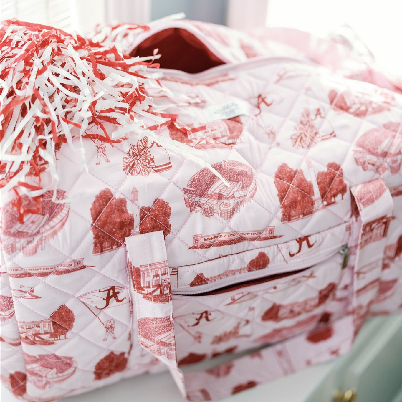 Light red quilted duffle bag with red University of Alabama symbols.
