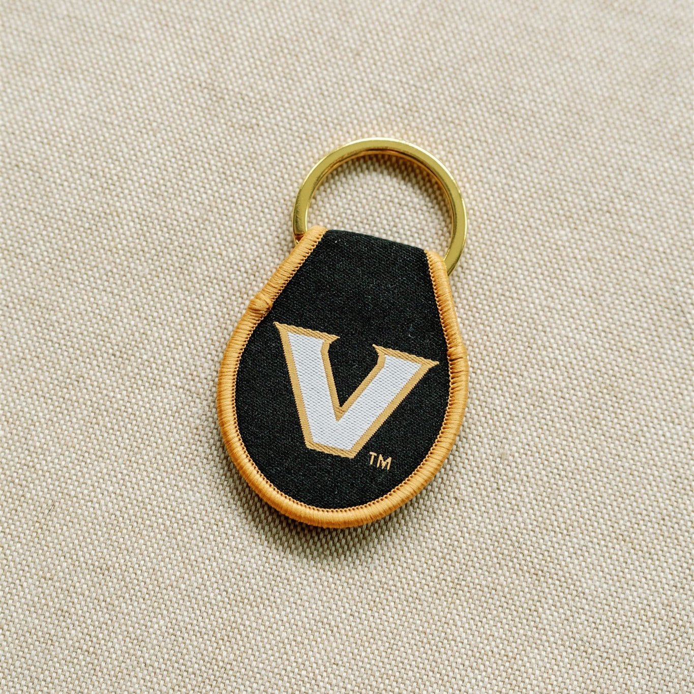 Black keychain with gold rim and Vanderbilt University logo embroidered in it.