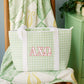 Green bag with Alpha Chi Omega Greek letters on a wooden chair against a patterned blanket.