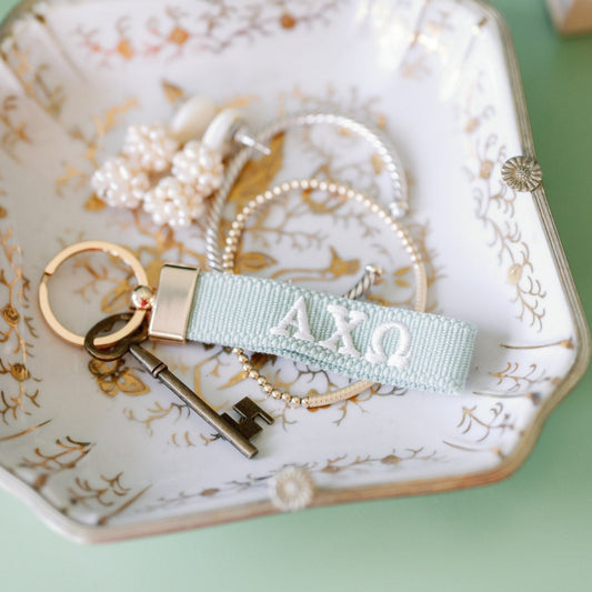 Light green keychain with Alpha Chi Omega Greek letters embroidered in white on a decorative plate.
