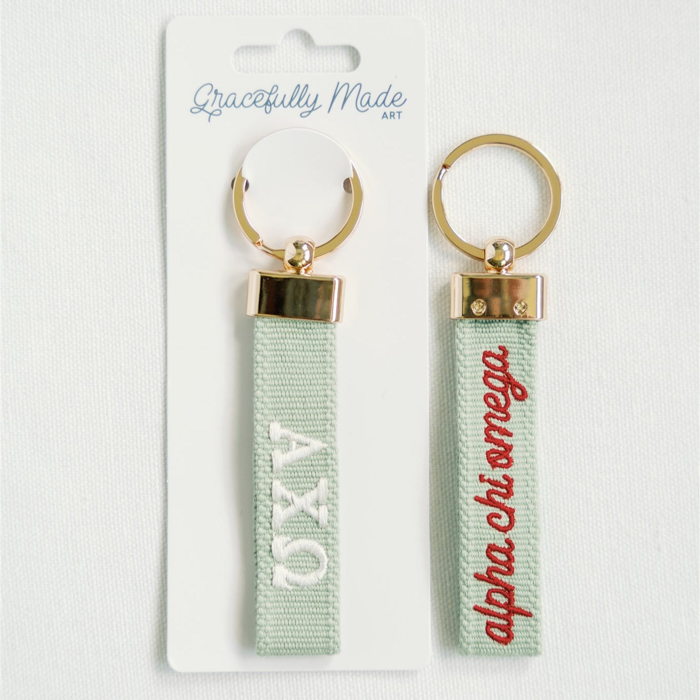 The front and back of the Alpha Chi Omega embroidered keychain. One side has the sorority name written out and one has the Greek letters.