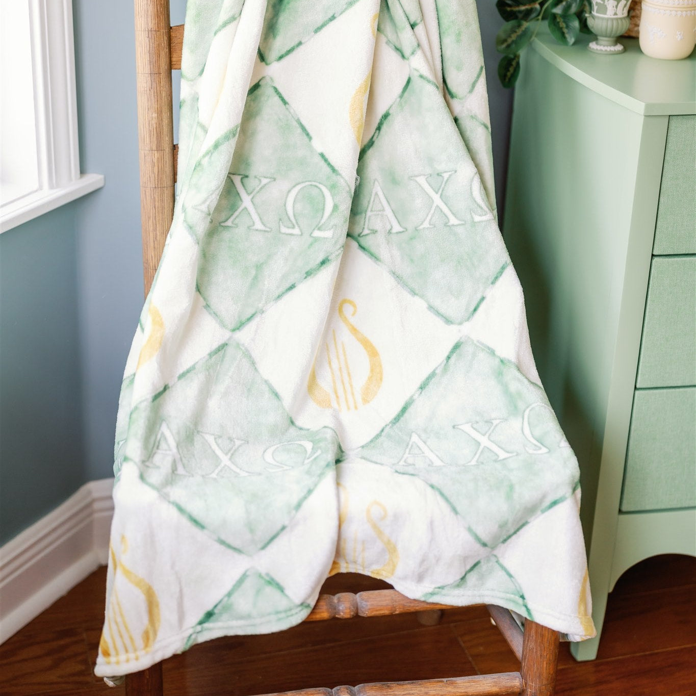 Green and white patterned blanket draped over a wooden chair against a gray wall.