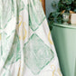 Blanket with Greek letters draped over a wooden chair against a light blue wall.