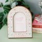 Decorative photo frame with 'Alpha Chi Omega' initials on a green surface with books and plants in the background.