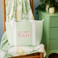 Green gingham tote bag with 'AXO' Greek letters sitting on a chair with the Alpha Chi Omega fleece blanket behind it.