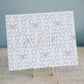 Watercolor art print with 'Alpha Delta Pi' Greek letters on a stand against a gray background