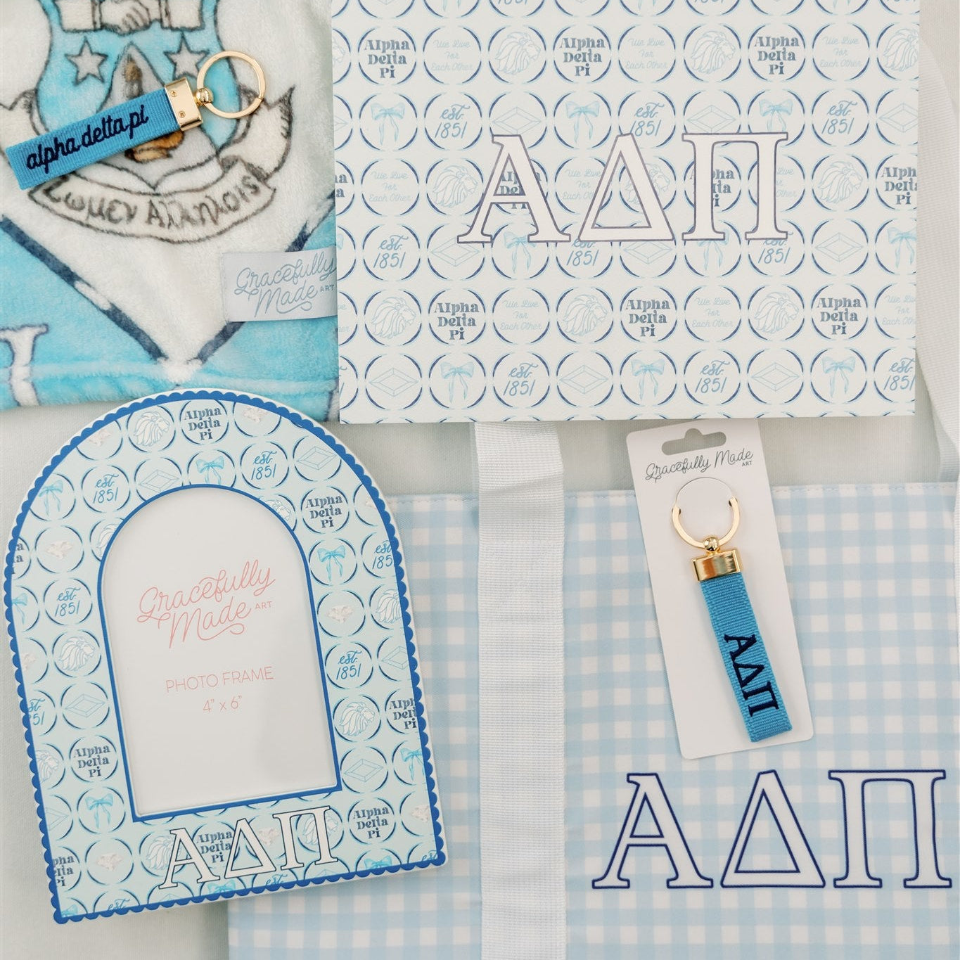 Collection of Alpha Delta Pi themed merchandise including a fleece blanket, keychain, and tote bag on a white background.