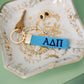 Blue keychain with Alpha Delta Pi Greek letters on a decorative dish with gold accents.