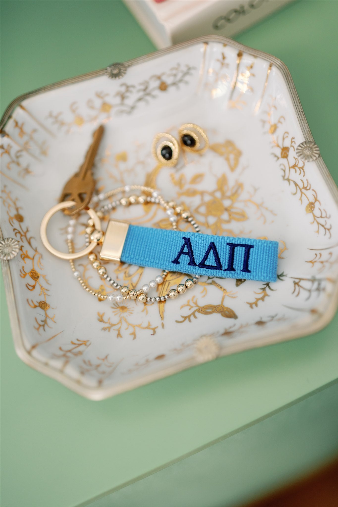 Blue keychain with Alpha Delta Pi Greek letters on a decorative dish with gold accents.
