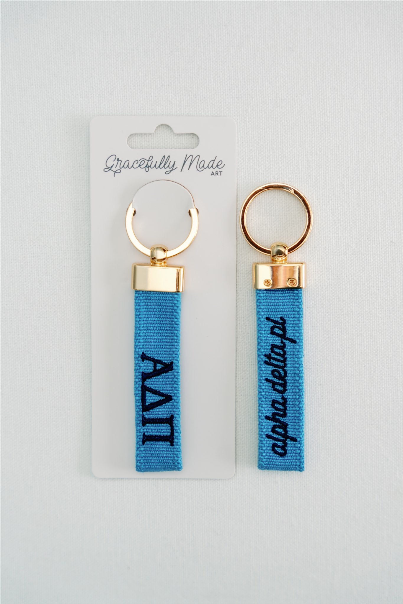 Front and back of blue Alpha Delta Pi keychains with gold rings on a white background, branded 'Gracefully Made Art'.