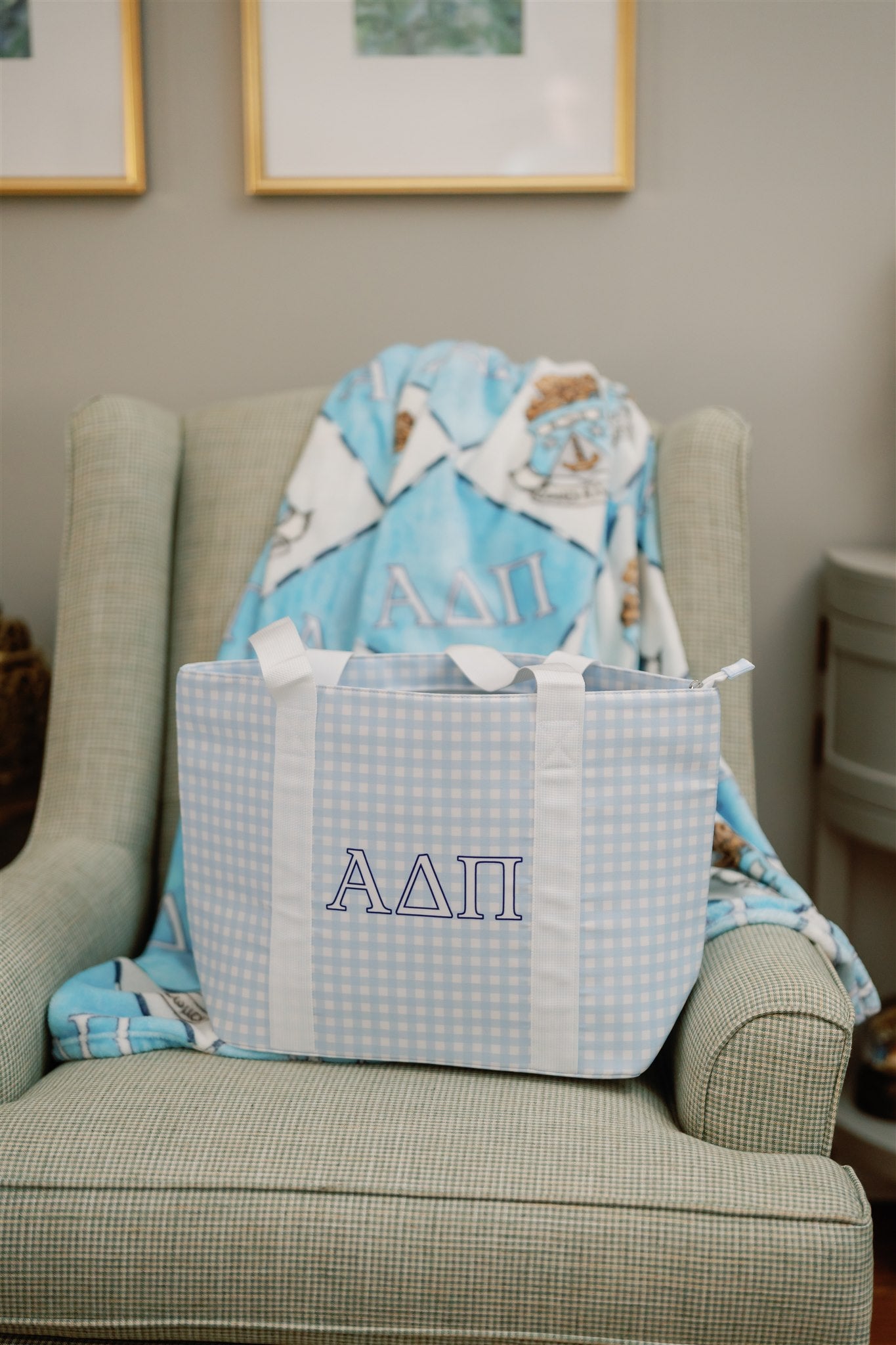 Blue gingham tote bag with Alpha Delta Pi Greek letters and white strap sitting on a chair.