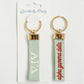 Pair of keychains with Alpha Gamma Delta Greek letters embroidered on a light green background