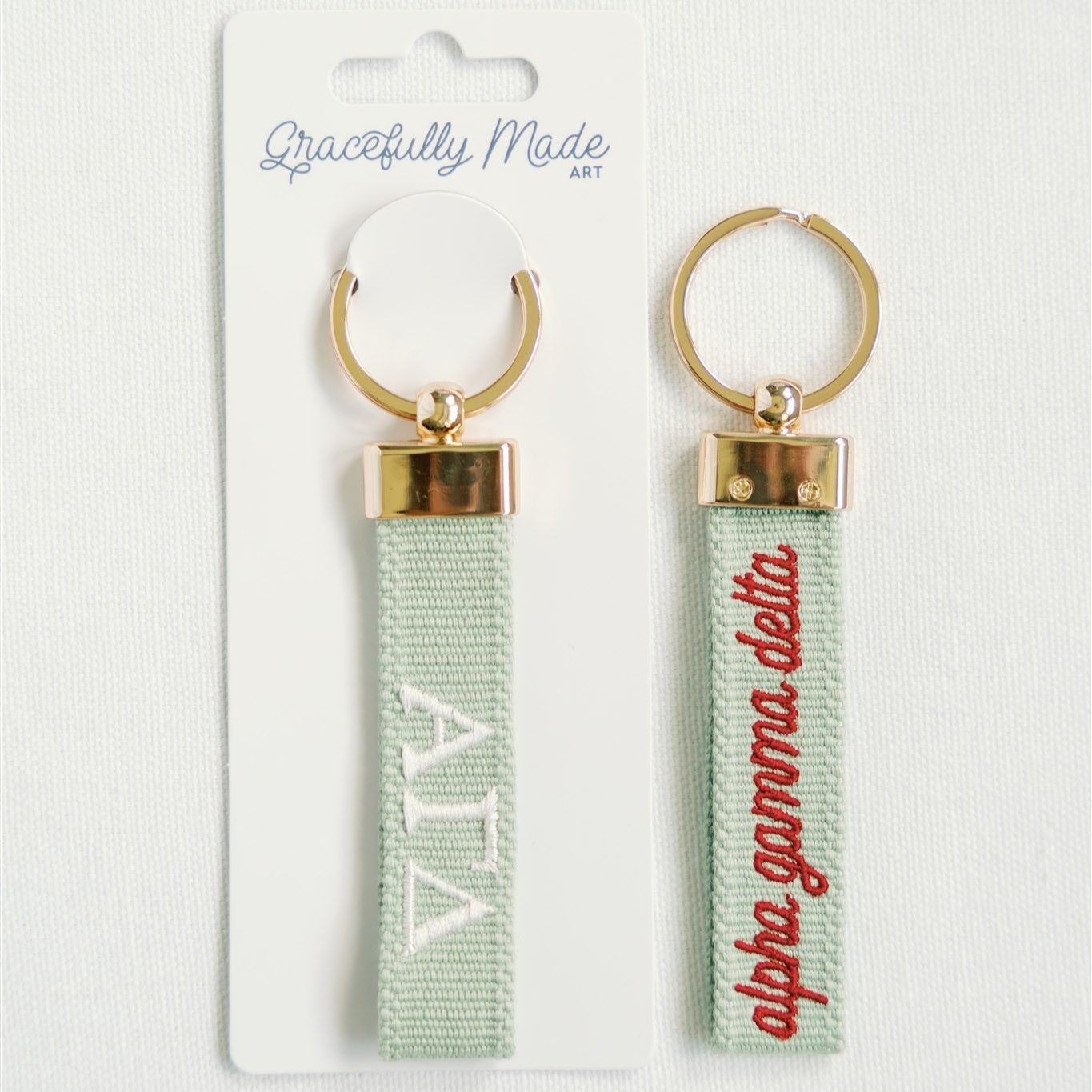 Pair of keychains with Alpha Gamma Delta Greek letters embroidered on a light green background